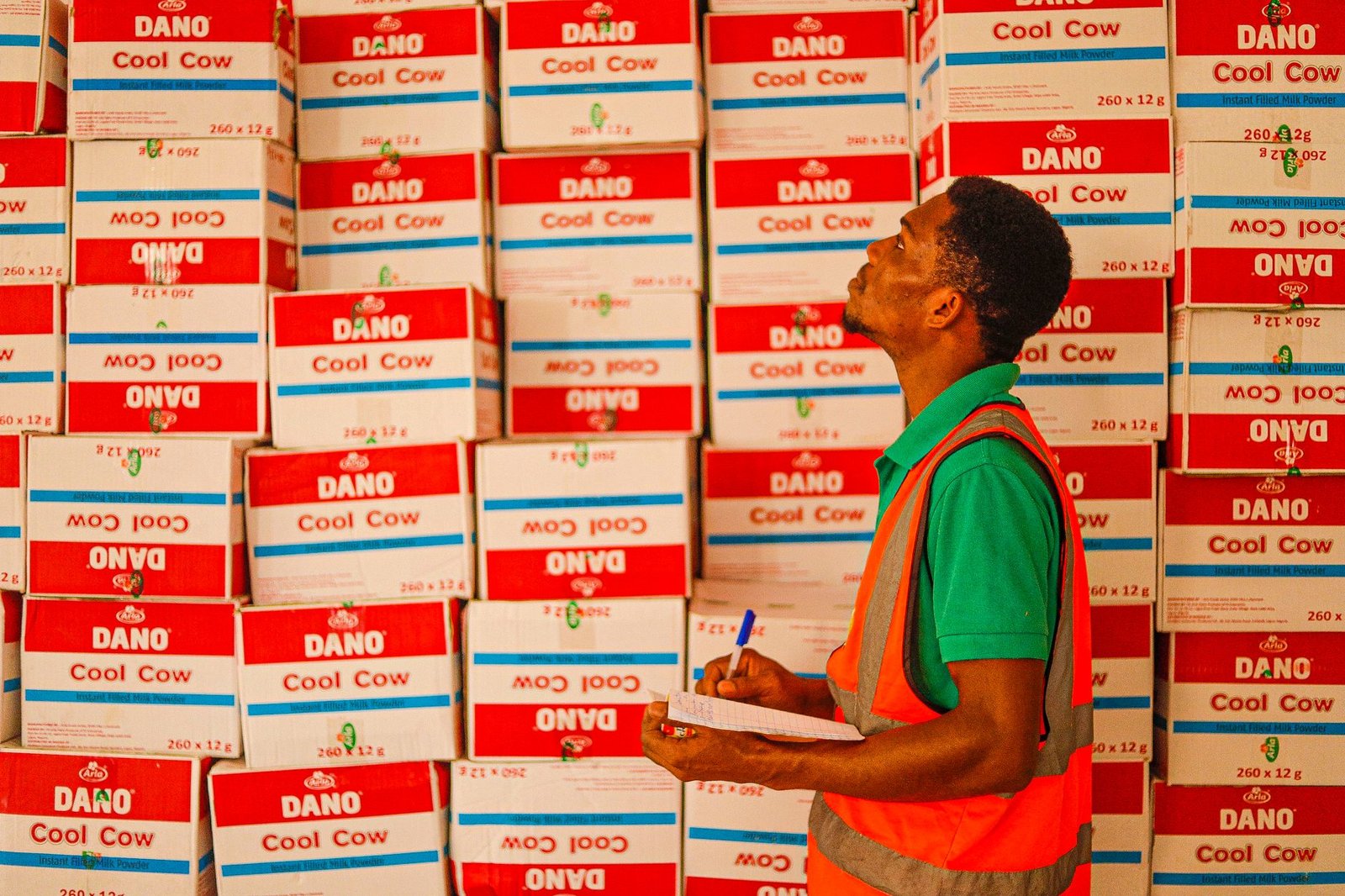 man working in a warehouse walking and looking at stack of boxes with a notepad